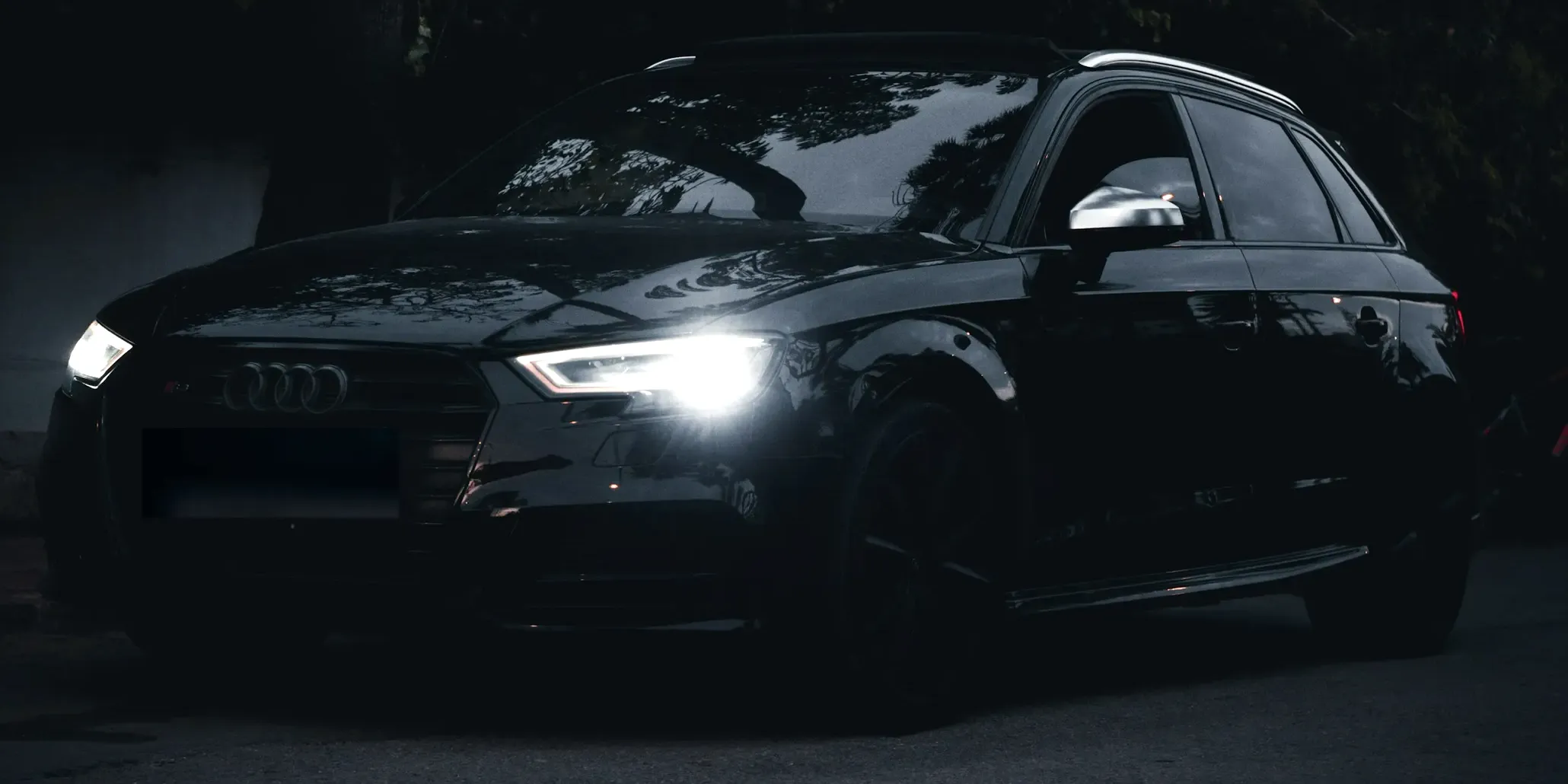 Crni Audi S3 Sportback fotografisan sprijeda pod uglom u mraku, sa upaljenim LED farovima